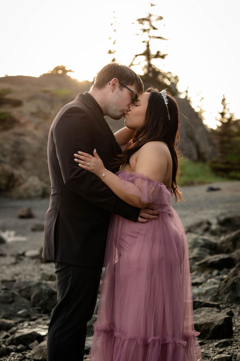 A couple shares a romantic moment at sunset on rocky terrain wearing formal attire.
