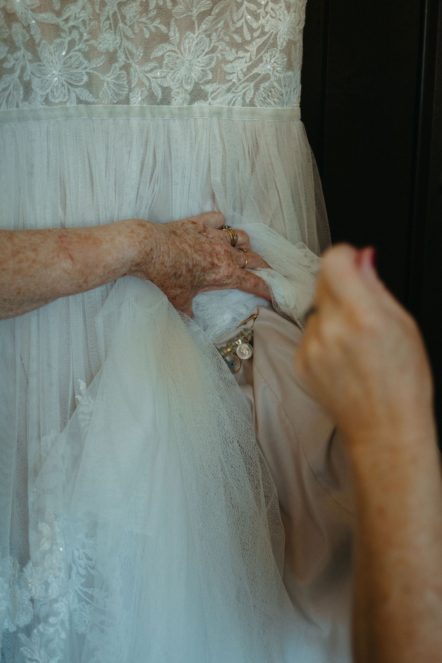 Close-up detail of intricate lace pattern on white wedding dress being adjusted.