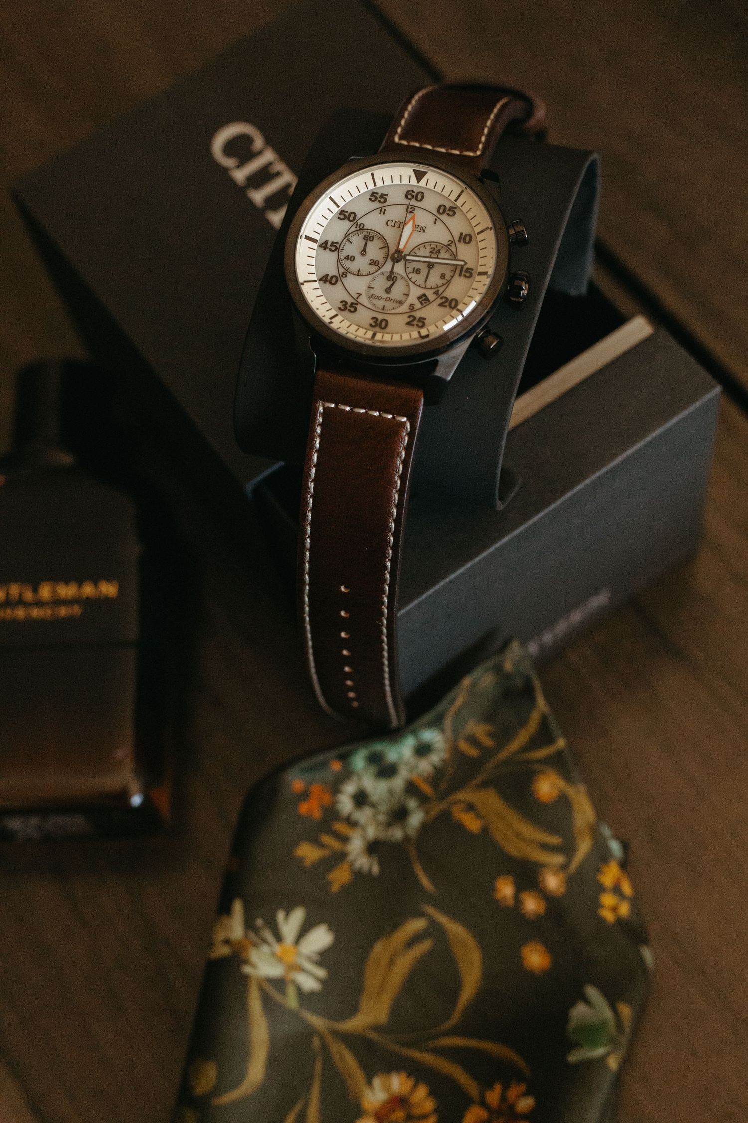 Elegant wristwatch with brown leather strap displayed on dark wooden surface with decorative items.