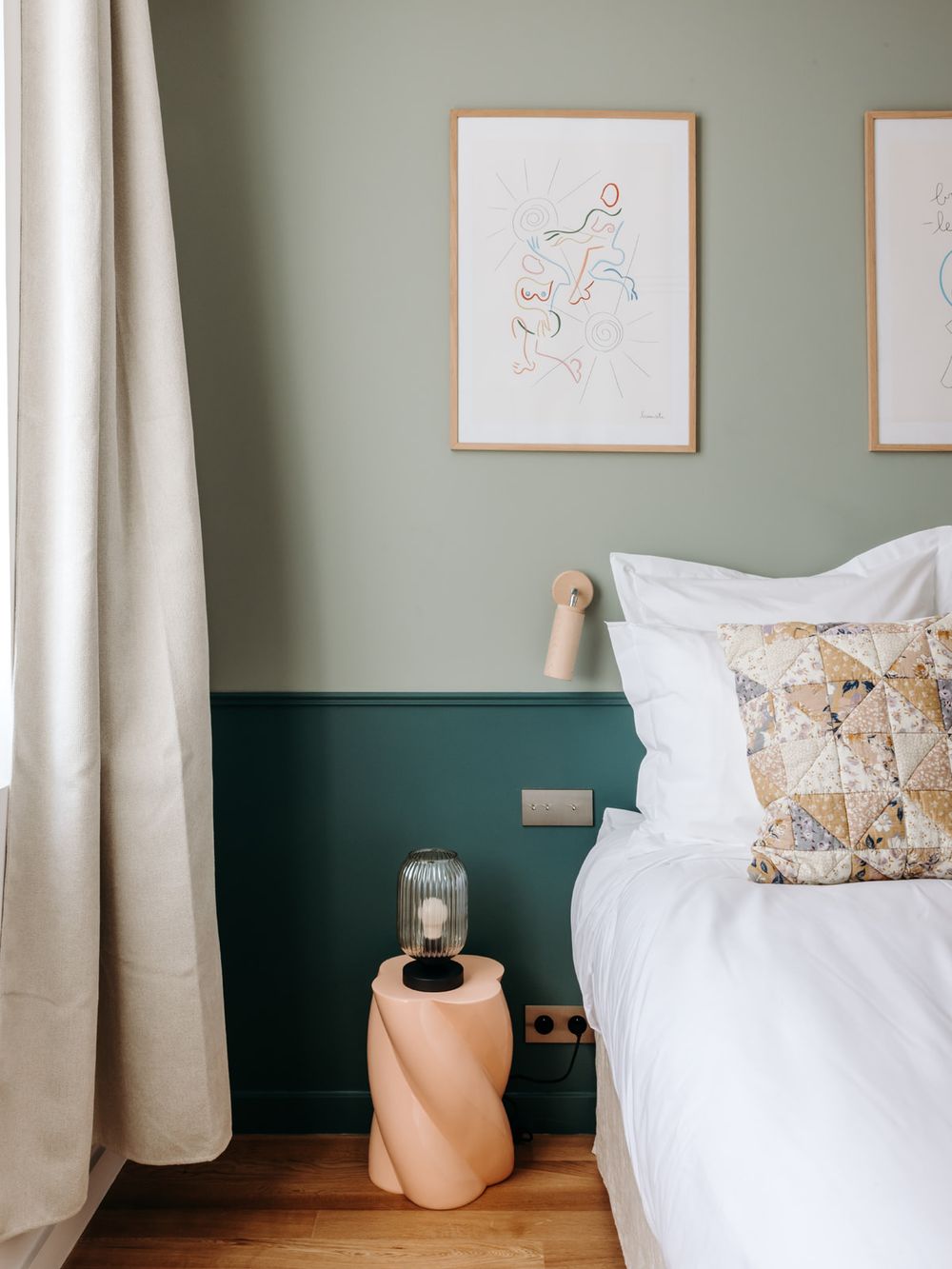Sage green two-tone bedroom with white bedding, peach side table, wall sconce, and abstract framed art above.