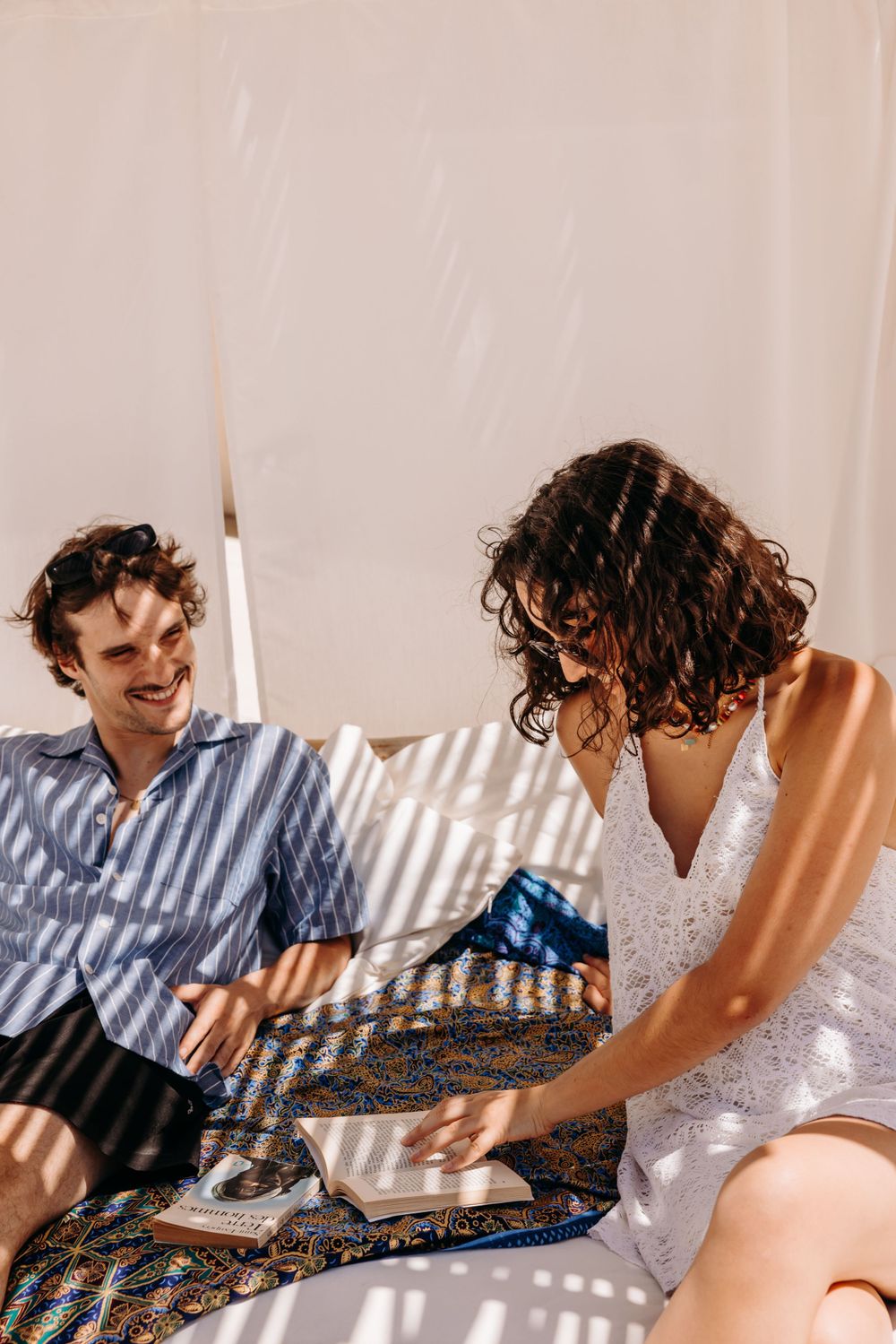 A couple enjoying a casual moment together on a patterned blanket in soft lighting.