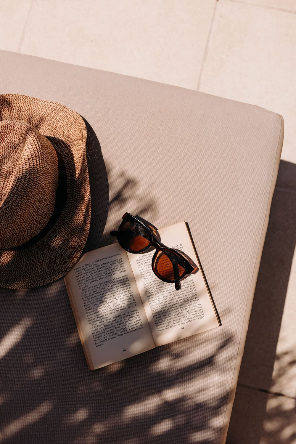 Straw hat and sunglasses on open book with dramatic shadows.