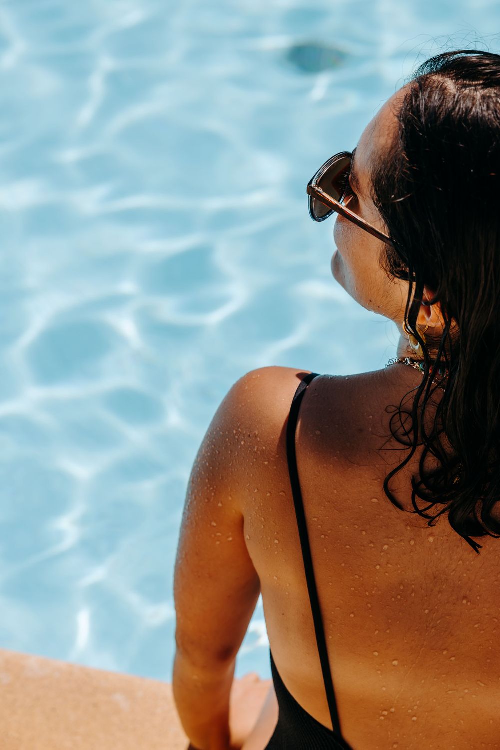Woman in black swimsuit relaxing by pool edge with blue water.