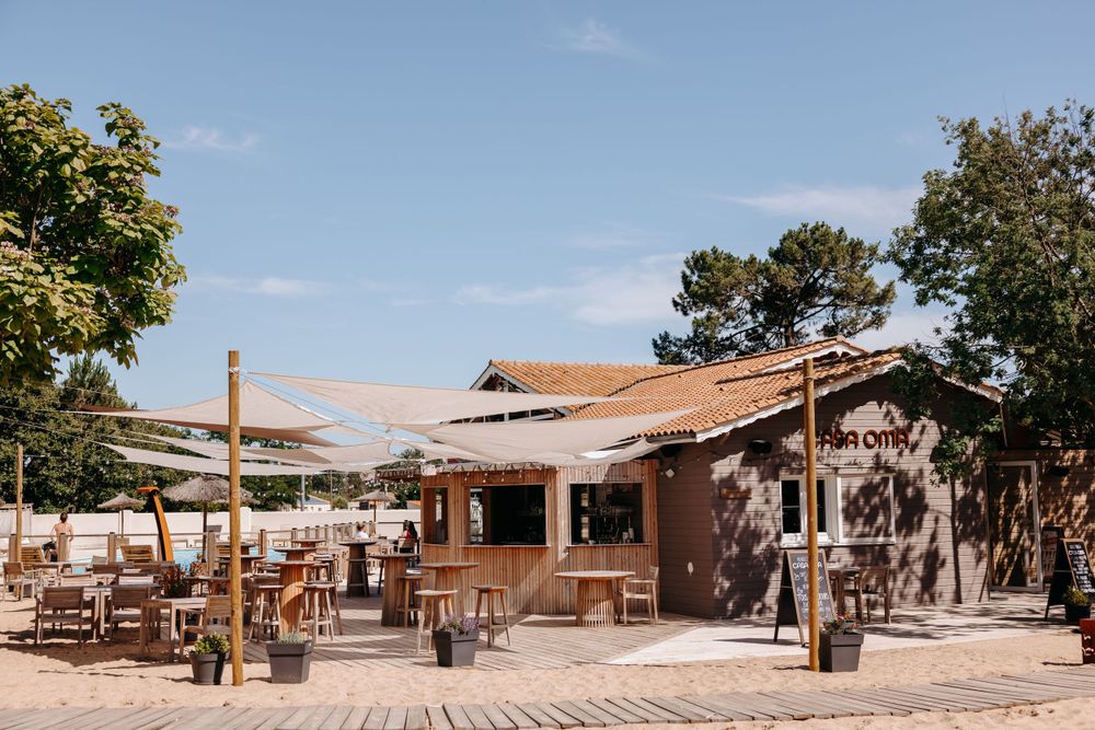 Rustic outdoor beach bar with wooden furniture and beige shade sails.