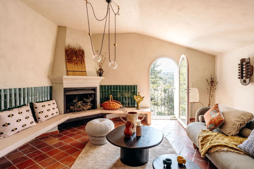 Cozy Mediterranean living room with terracotta tiles, arched window, green tile fireplace, and modern black coffee table.