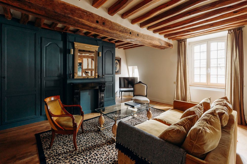 Cozy French living room featuring exposed ceiling beams, teal painted fireplace, leopard print rug, and velvet sofa.