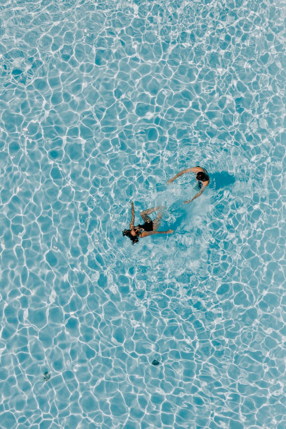 Aerial view of swimmers in clear turquoise pool water with ripple patterns.