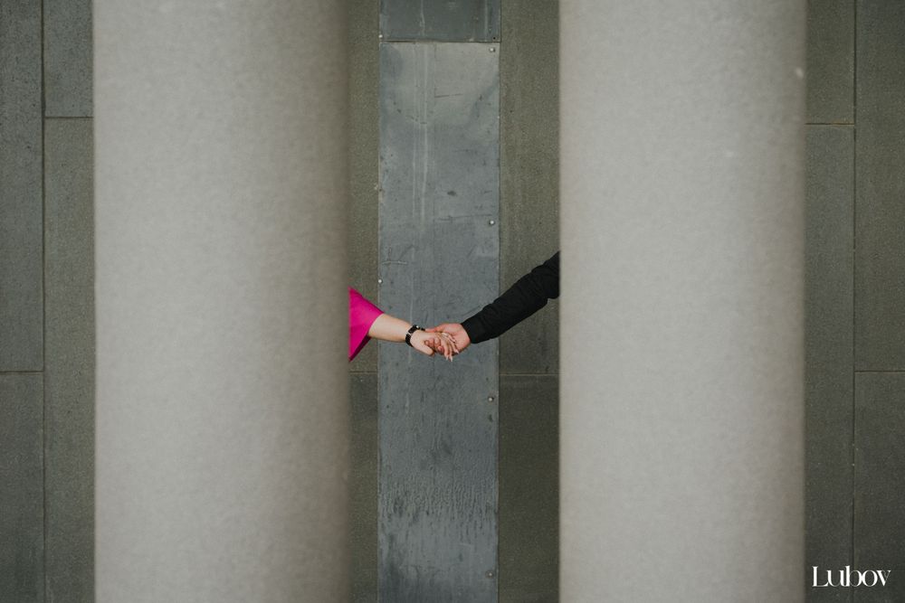 Two hands reaching between concrete pillars, one wearing pink, creating minimal composition.