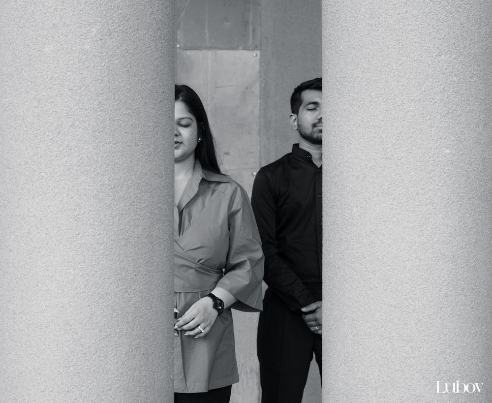 Black and white portrait showing two people standing back to back between columns.