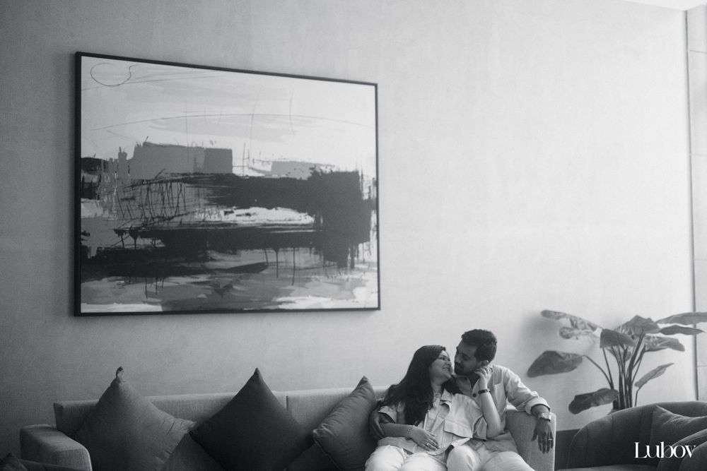Intimate black and white photograph of a couple on a couch beneath framed artwork.