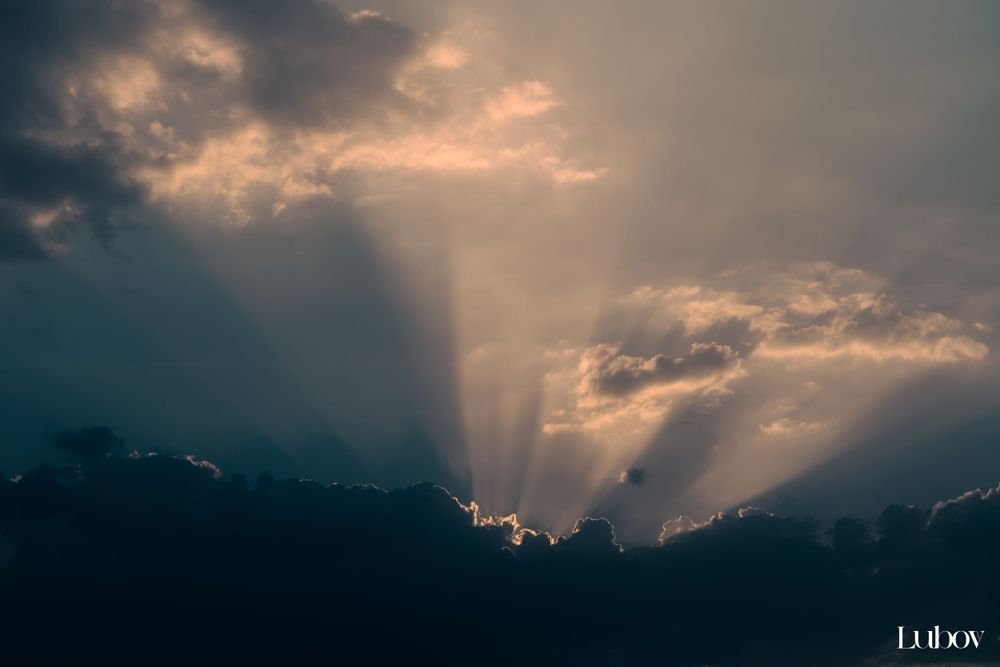 Dramatic sunset sky with sunbeams breaking through dark storm clouds.