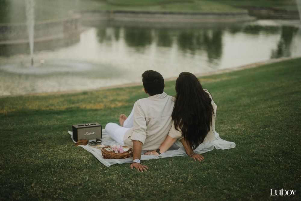 Romantic lakeside picnic scene with couple sitting on blanket near fountain.