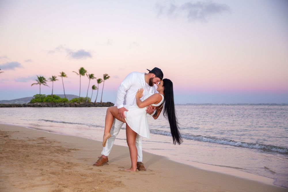 Romantic couple embraces on tropical beach at sunset with palm trees and ocean waves at Waialae Beach in Kahala.