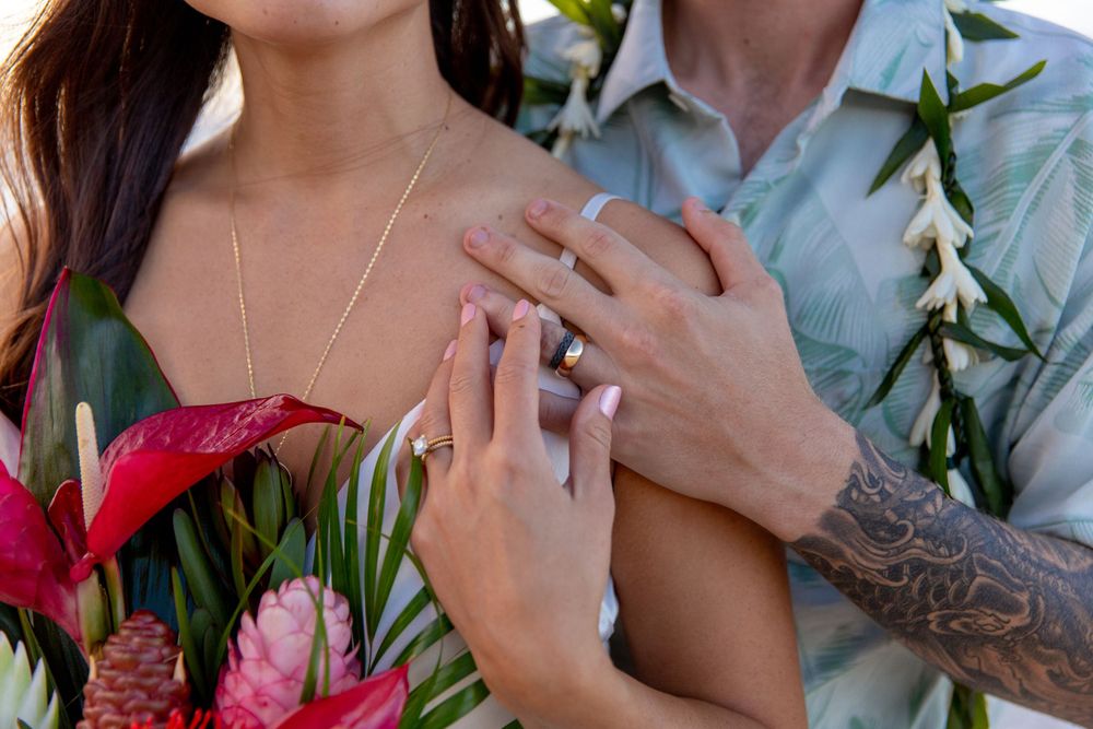 Close up of hands with engagement ring and tropical flowers including red anthurium and pink protea blooms.