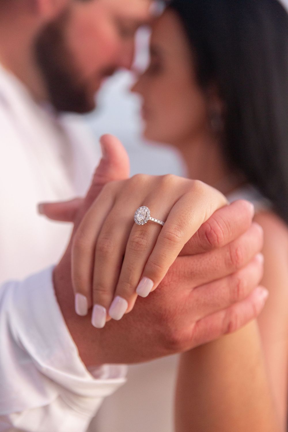 Close-up of hands clasped together showing an elegant diamond engagement ring with white manicured nails.