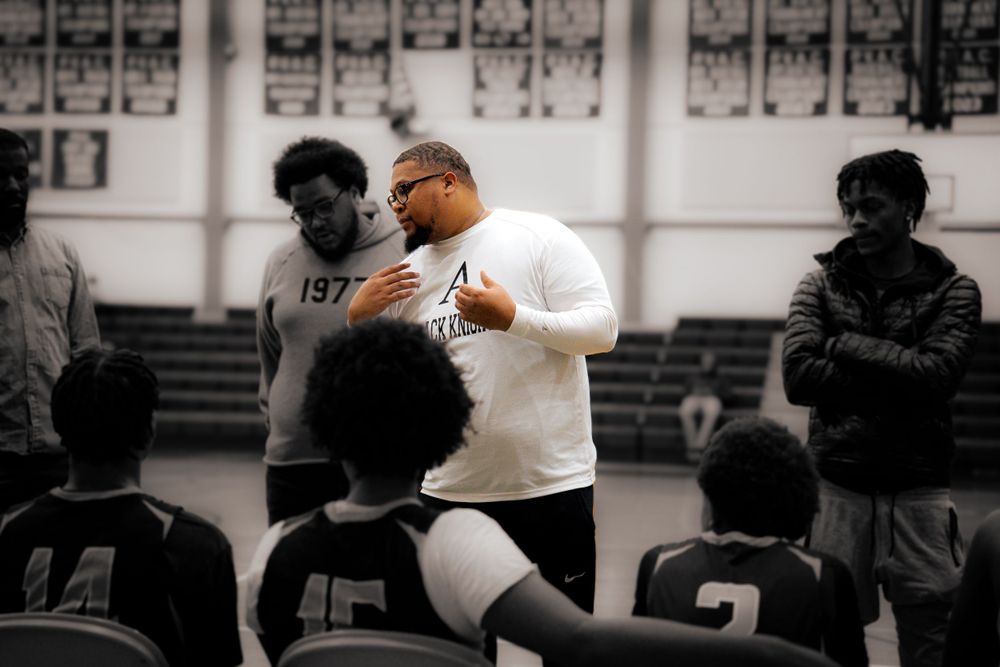 Basketball coach addresses players in huddle during indoor practice session.