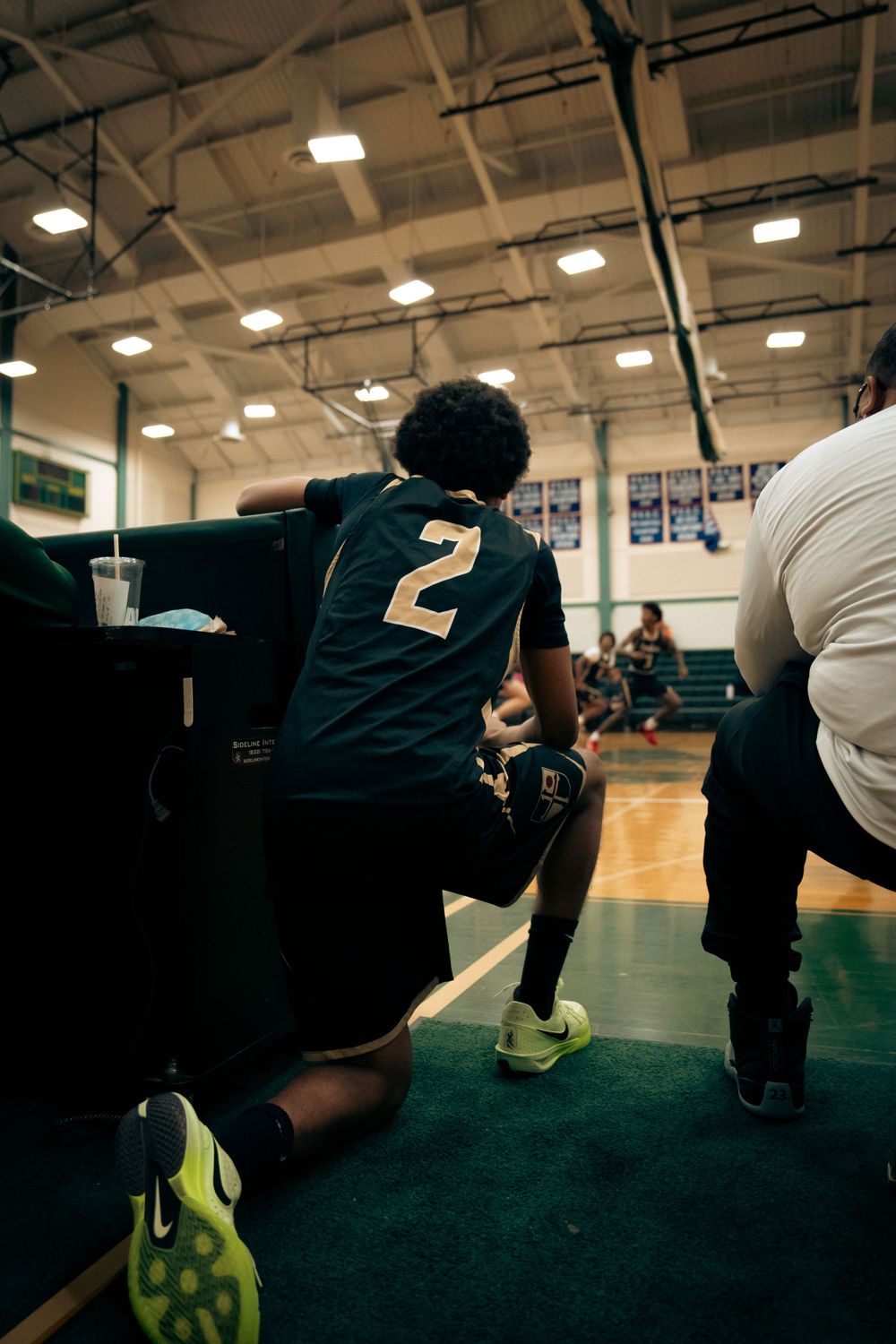 Youth basketball player wearing number 2 jersey kneels courtside during a game timeout.