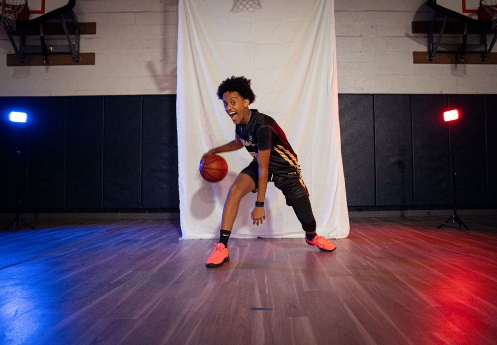 Young basketball player dribbles in front of white backdrop with red and blue studio lights.