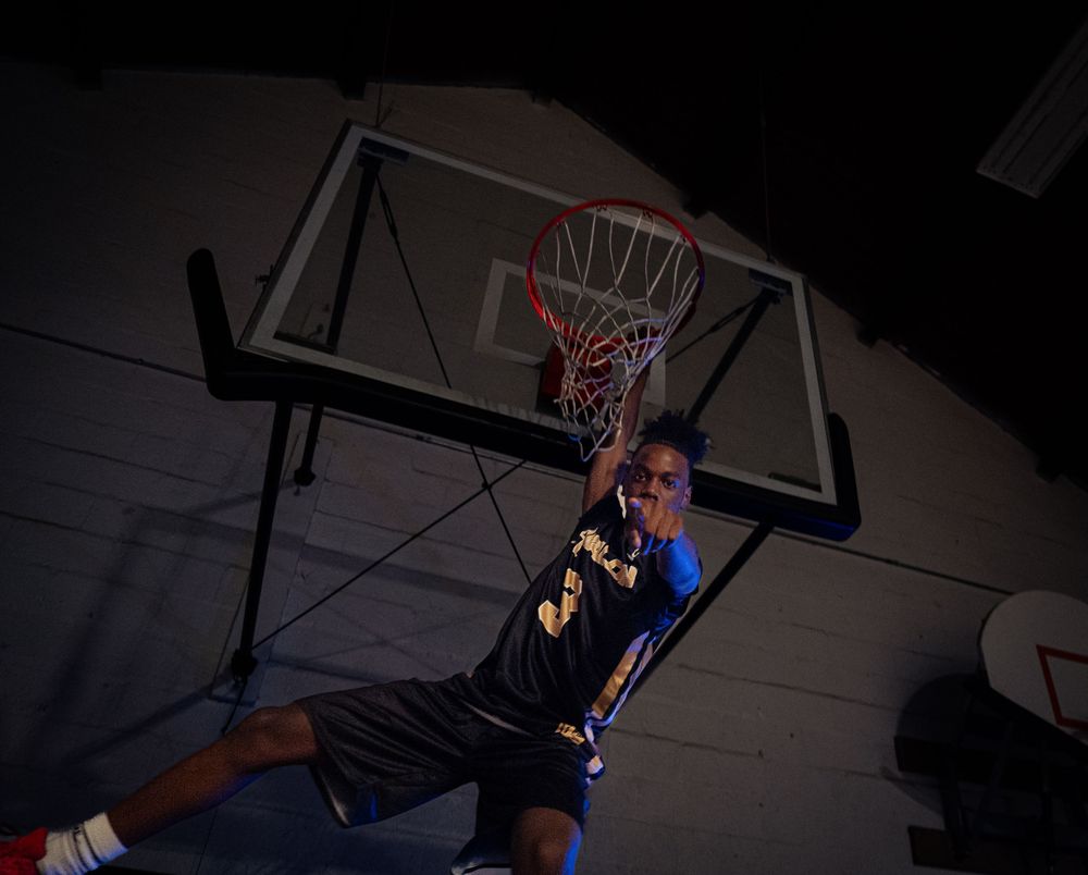 Basketball player dunks ball on indoor hoop in dramatic low-light action shot.
