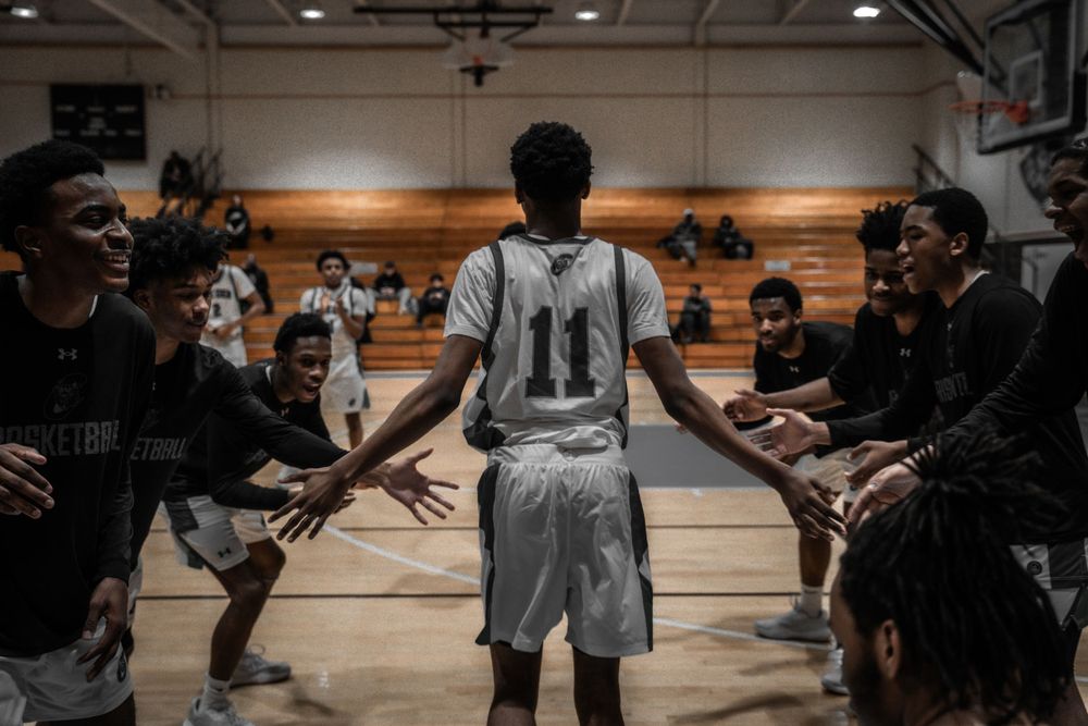 Basketball player in number 11 white jersey receives high-fives from teammates in a gymnasium.