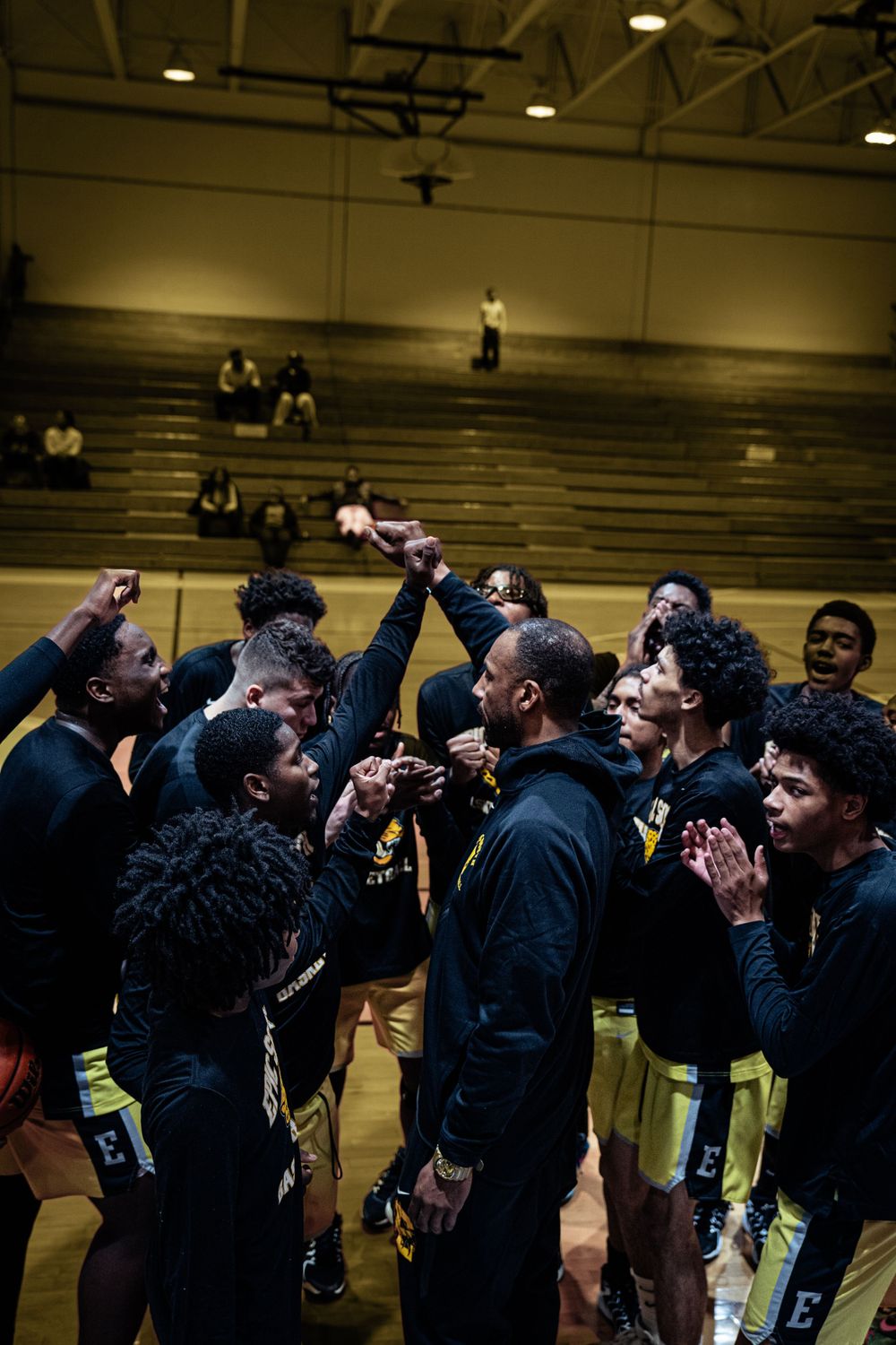 Basketball team huddles with coach on indoor court during motivational team meeting.