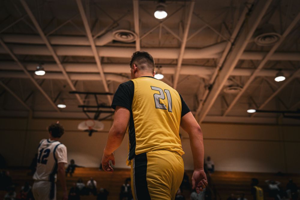 Basketball player wearing yellow number 21 jersey walks on indoor court during game.