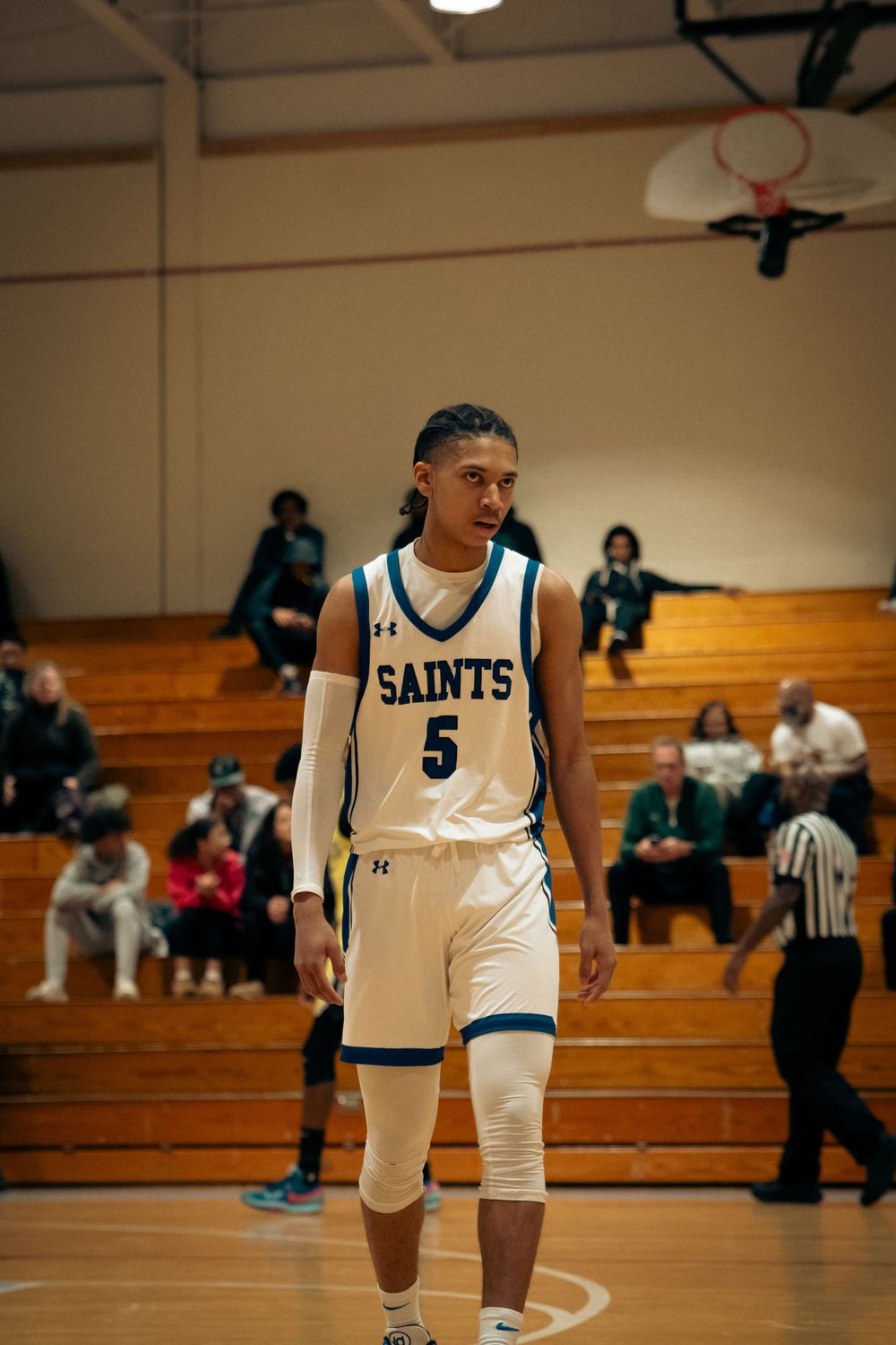 Basketball player number 5 in white Saints jersey walks on indoor court during game.