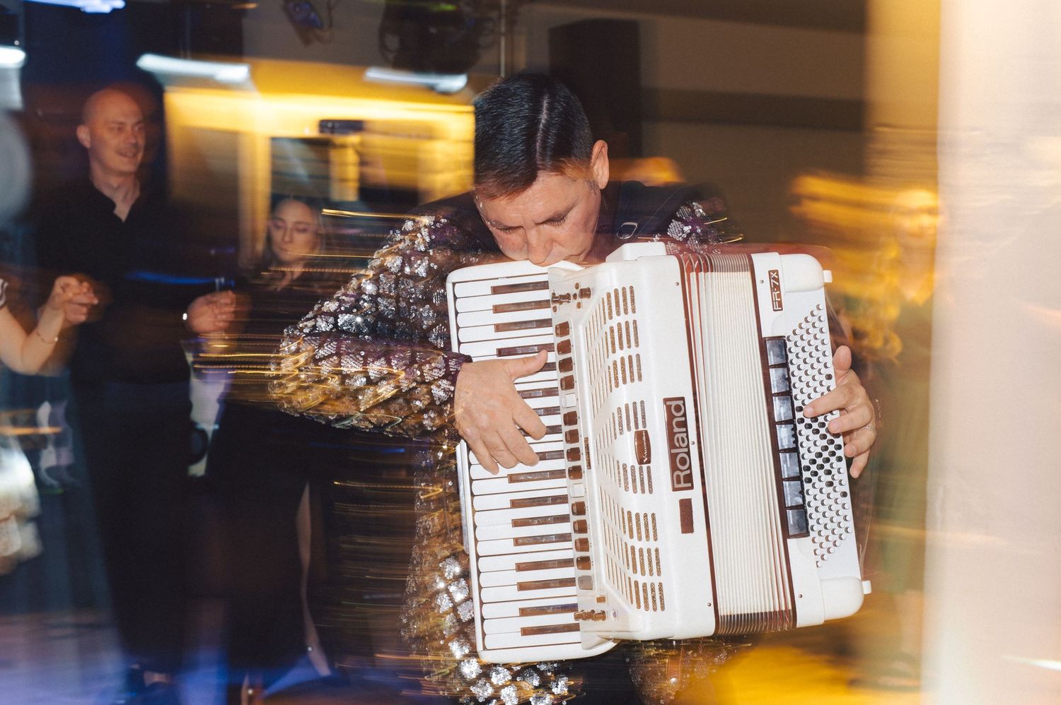A musician plays a white accordion during a lively performance at an indoor venue with motion blur effects.