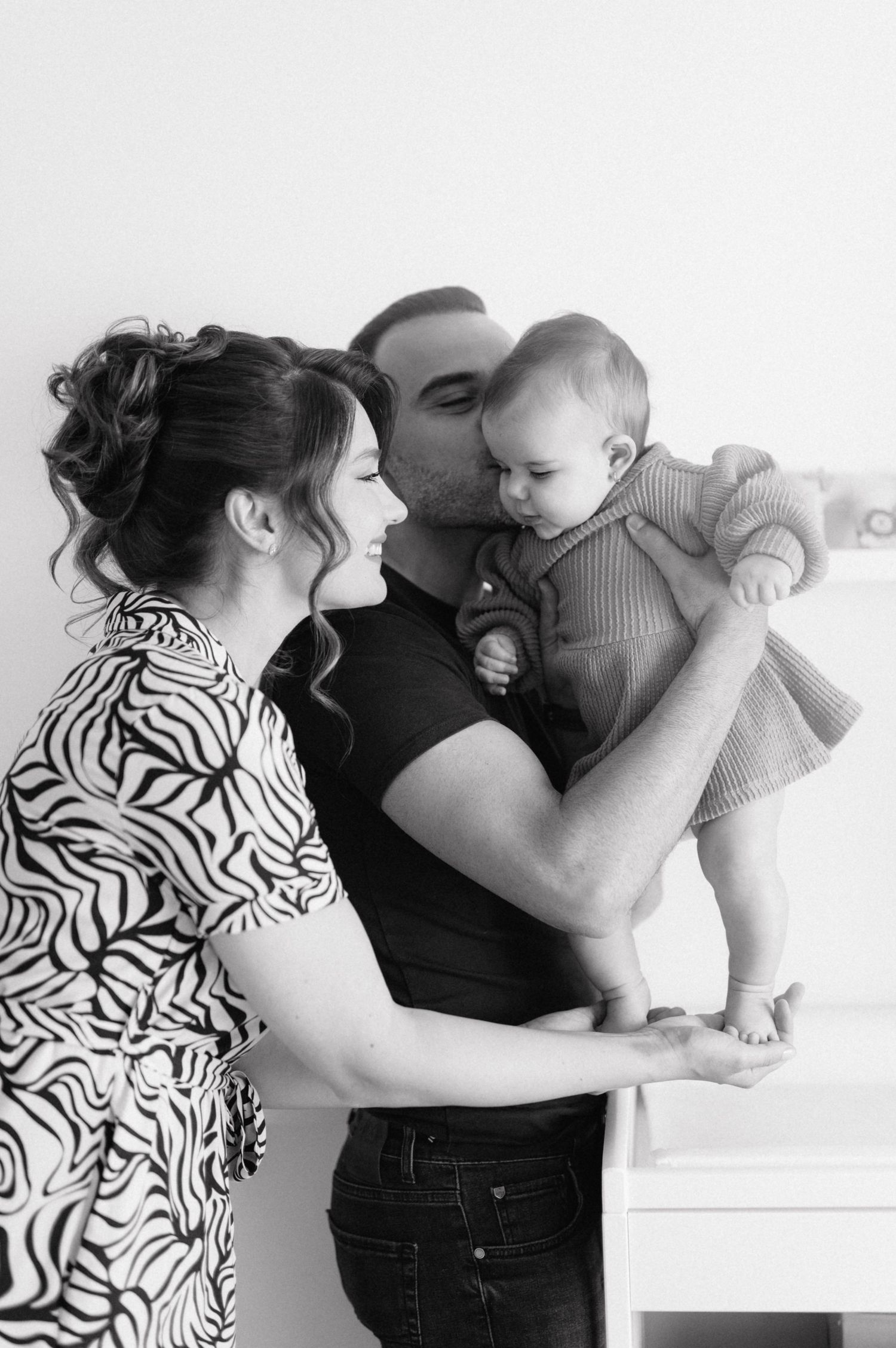 A black and white portrait of a happy family moment featuring a baby wearing light striped clothing.
