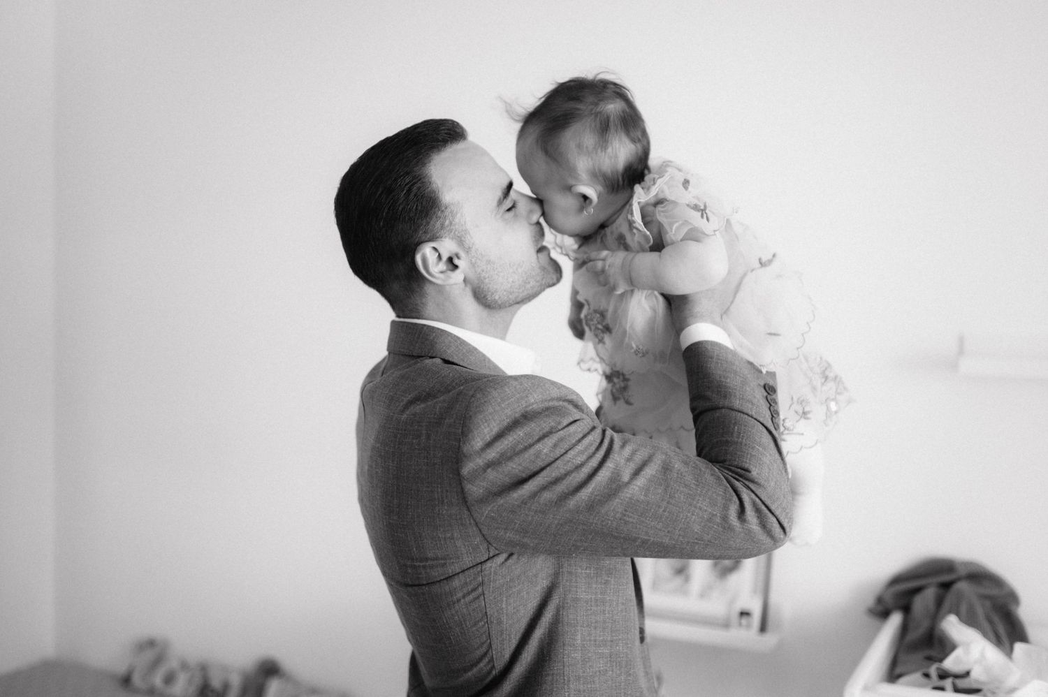 A tender black and white vintage photograph shows a suited man lifting a small baby in the air.