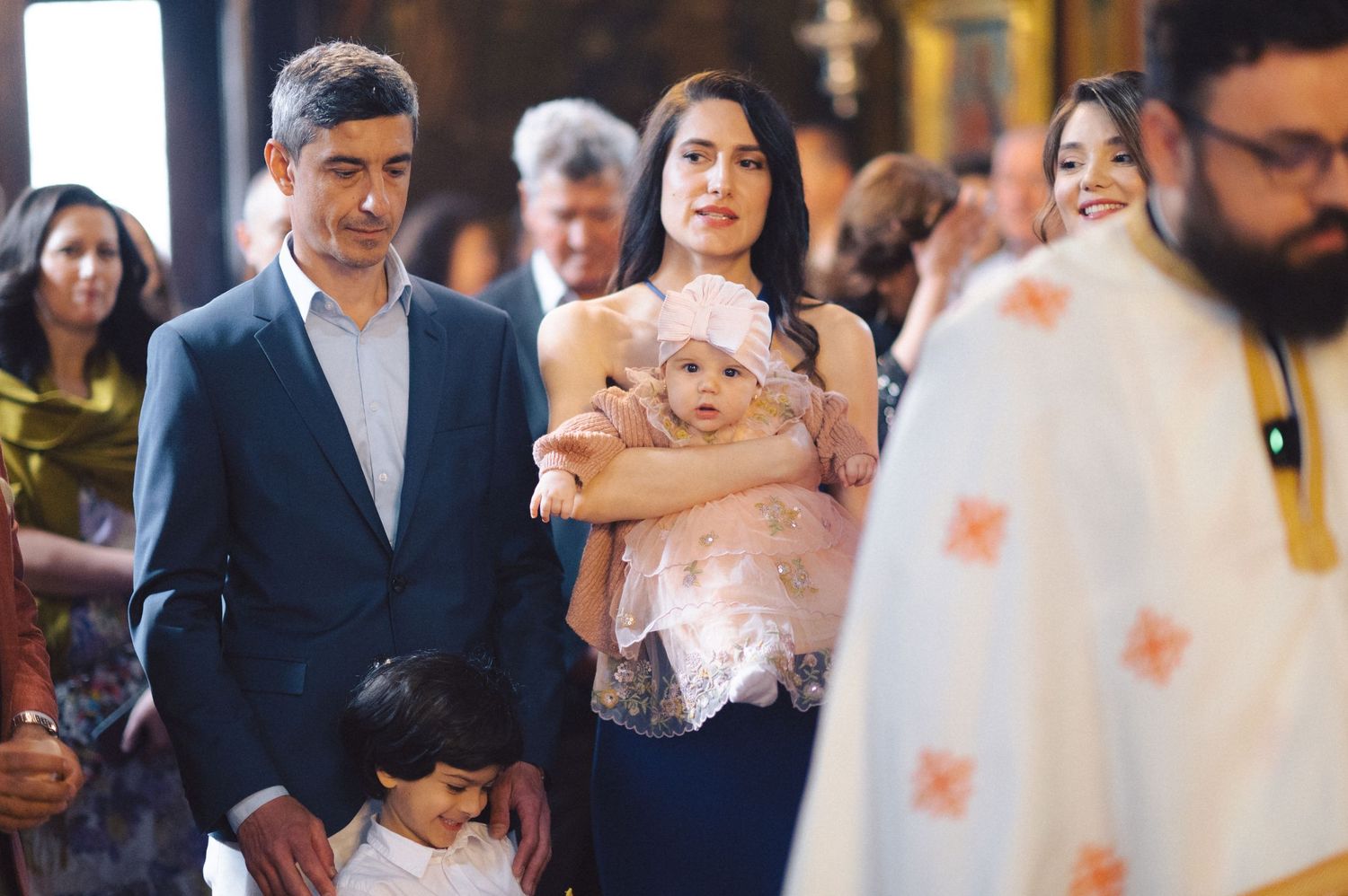 A young family participates in a traditional Christian baptism ceremony inside an ornate church.