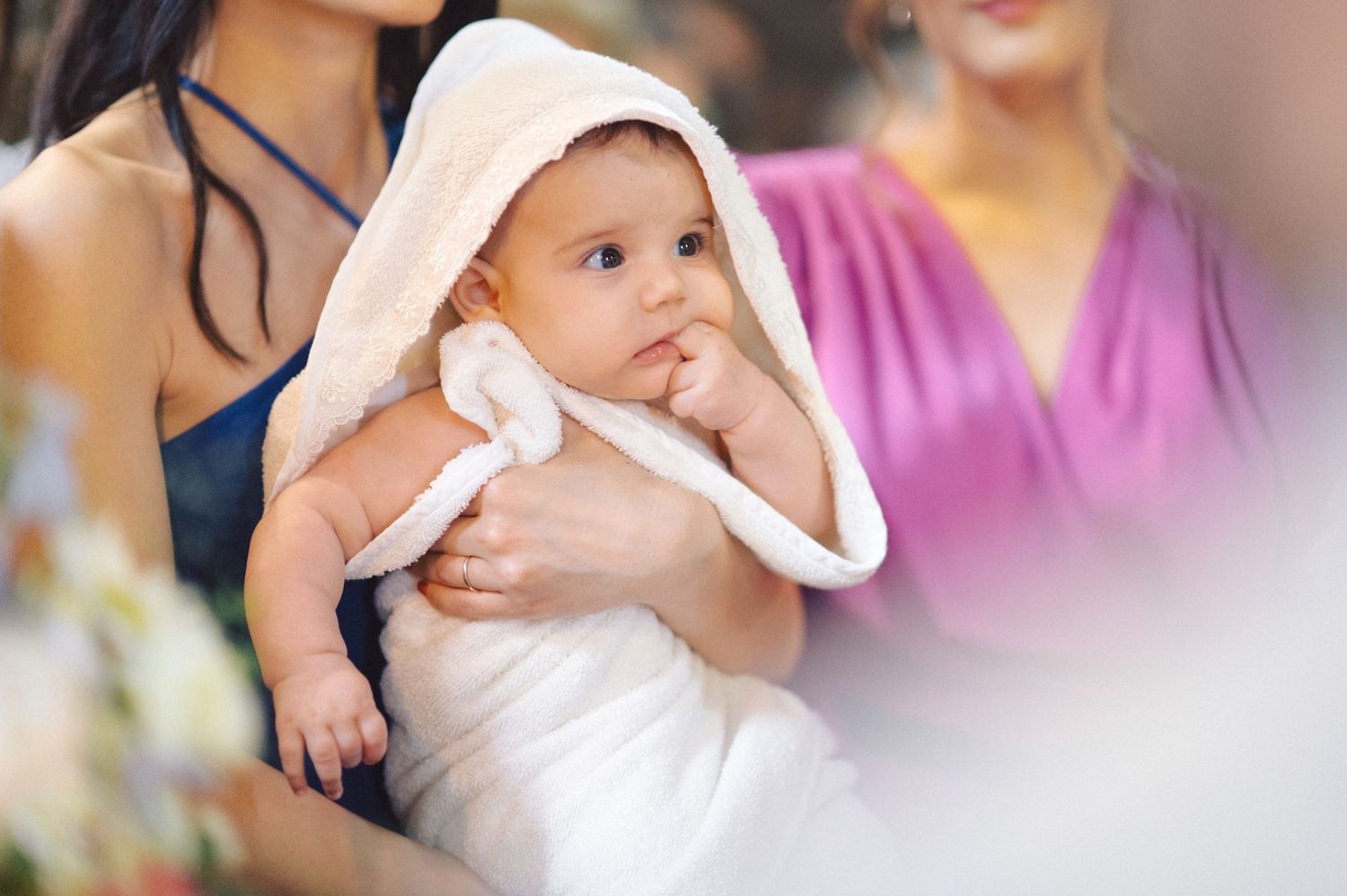 A baby in white baptismal clothing looks on curiously during a church ceremony.
