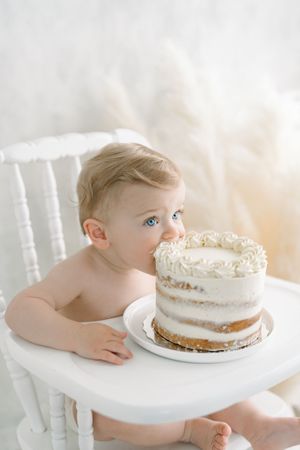 Bébé mangeant à pleine bouche son gâteau d’anniversaire dans un décor lumineux et minimaliste