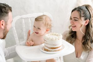 Parents et bébé riant ensemble lors d’une séance anniversaire avec gâteau lumineuse et épurée
