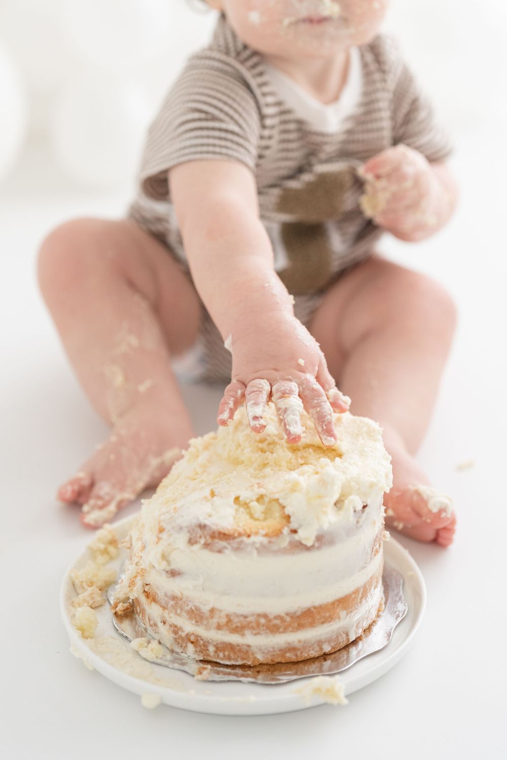 Plan rapproché sur les petits doigts plein de crémage d'un gâteau fait pour une séance premier anniversaire au studio dans un décor lumineux