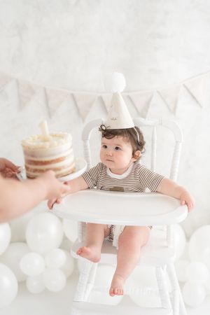 Enfant assis dans une chaise haute antique qui reçoit son gâteau d'anniversaire dans un décor lumineux avec fanions de lin