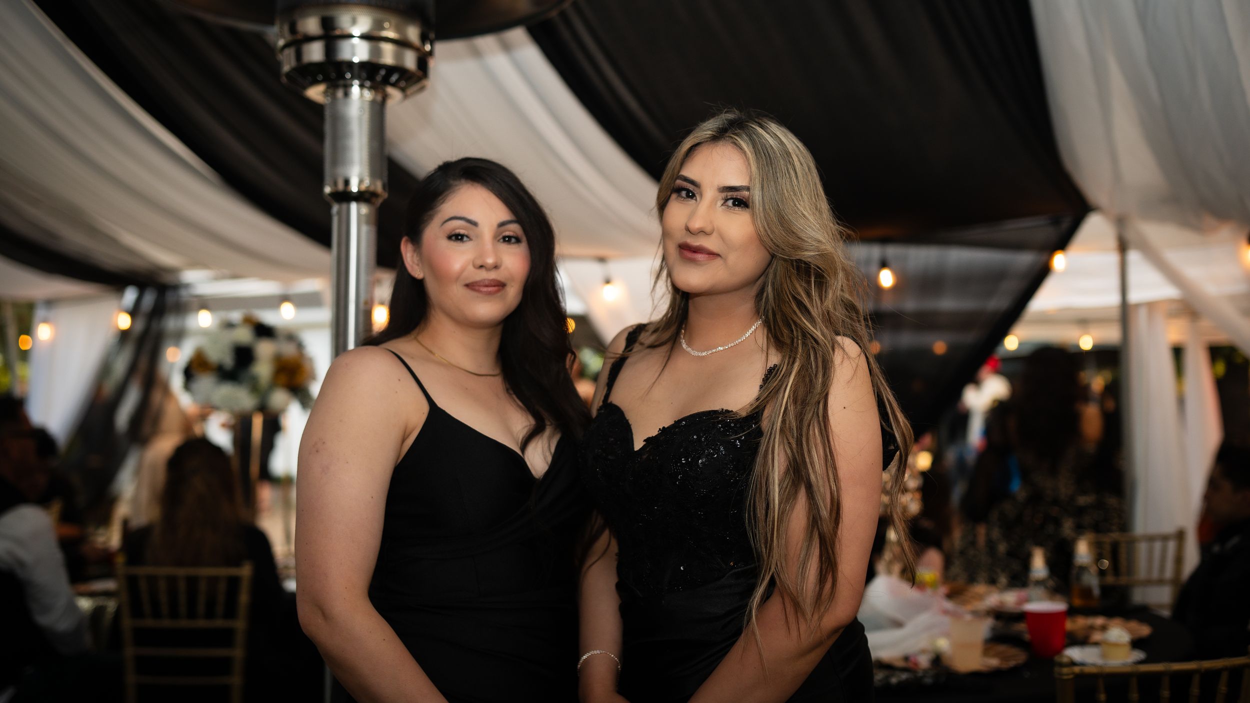 Guests mingle and socialize at an elegant evening event under a white tent with decorative lighting.