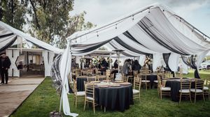 White wedding tent reception setup with rustic wooden tables and chairs arranged on a grassy lawn for outdoor dining.