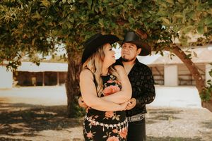 A romantic couple embraces under sunlit trees during a golden hour photoshoot in a rustic outdoor setting.