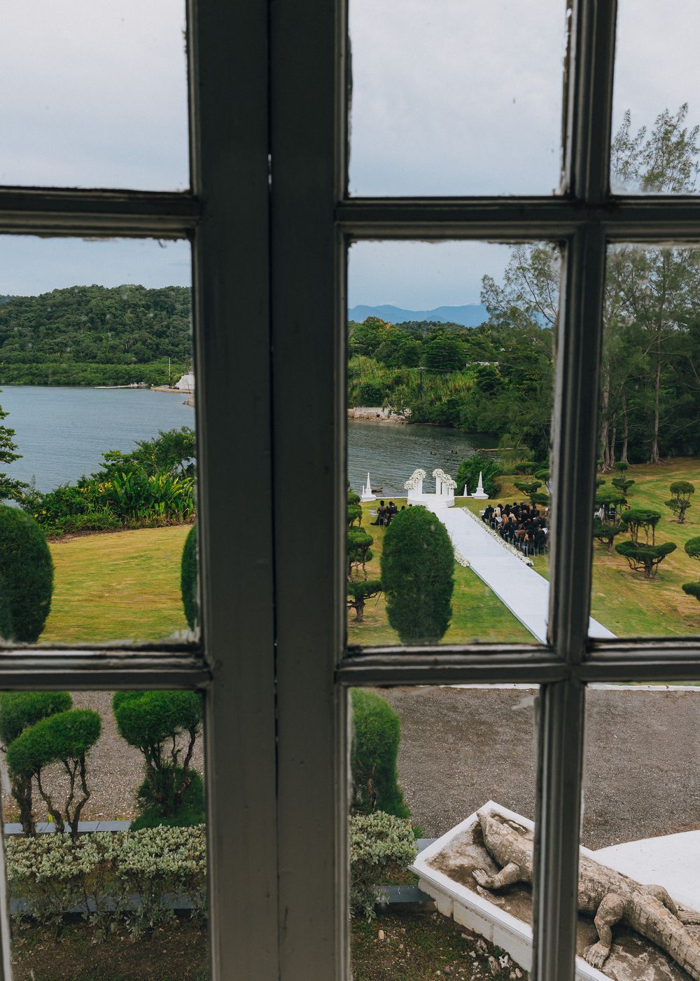 View through black window frames overlooking a scenic coastal landscape with rolling hills and water in the distance.