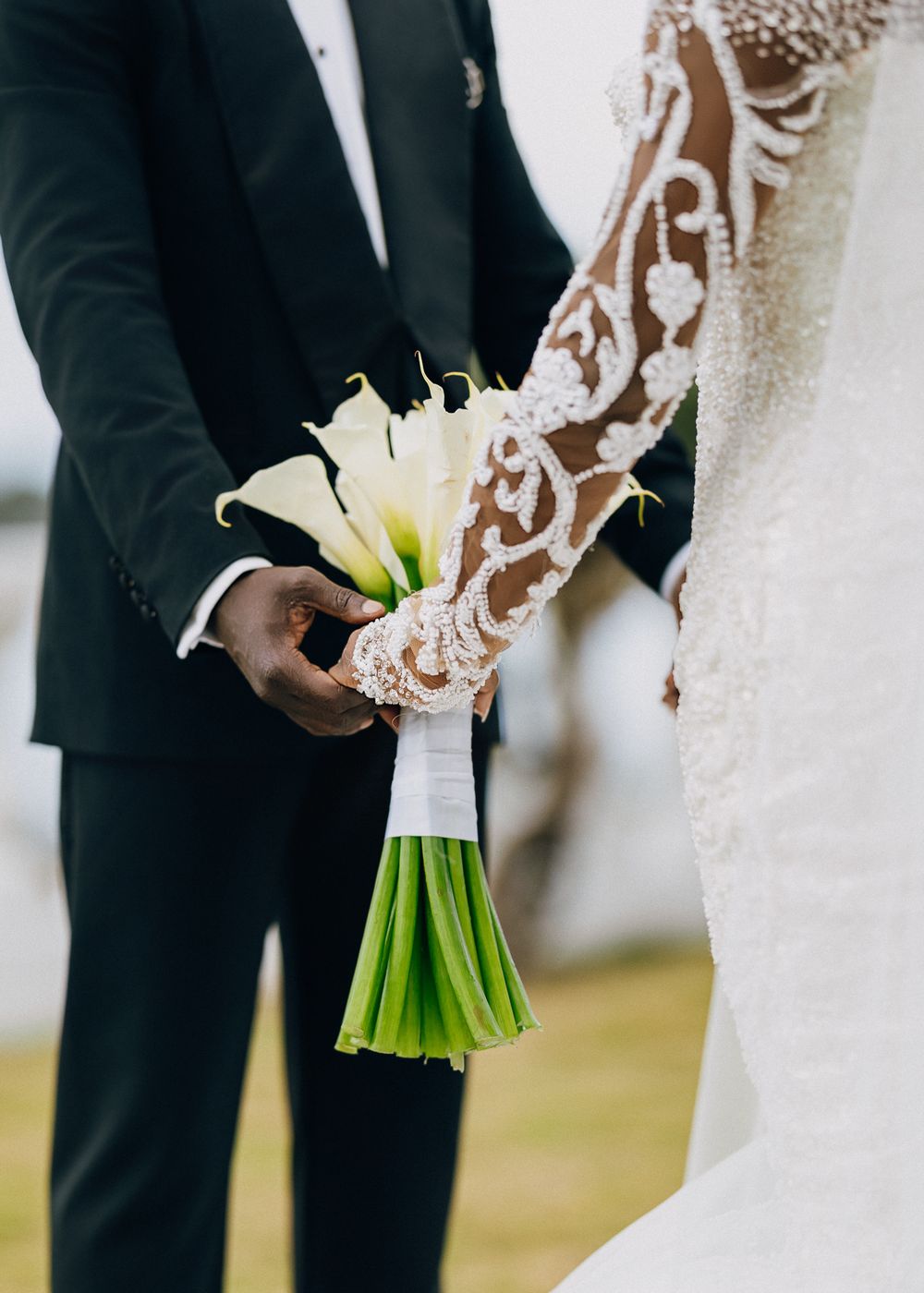 Close-up of a wedding bouquet with white calla lilies and wrapped stems being held between bride and groom.