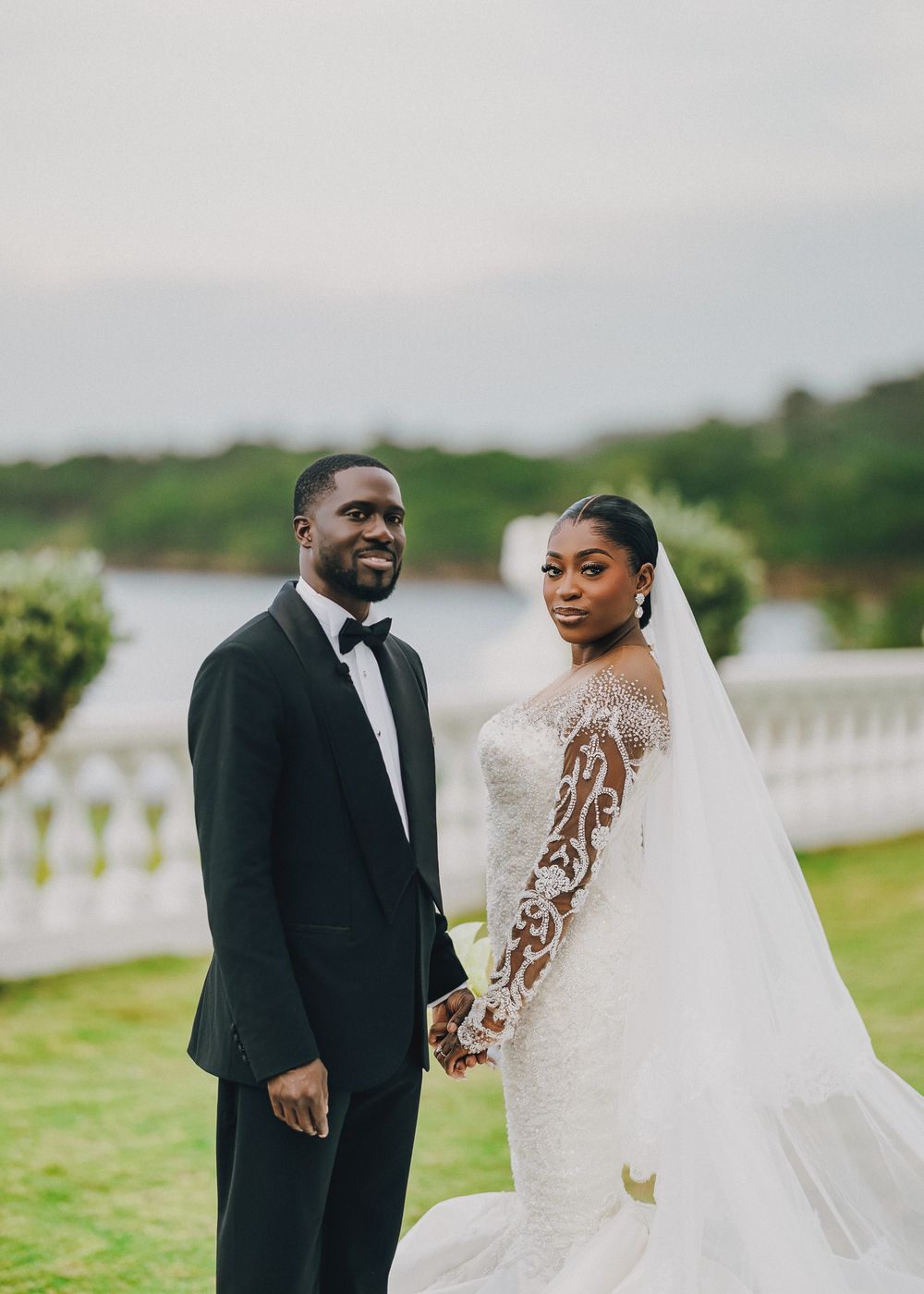 A joyful wedding couple shares a candid moment outdoors on their special day, with the bride wearing a detailed lace gown.