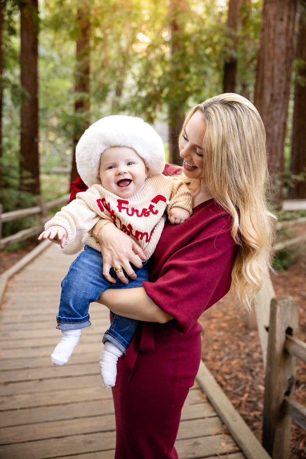 A joyful interaction between a Bay Area mom and baby on a wooden boardwalk in a redwood forest setting.