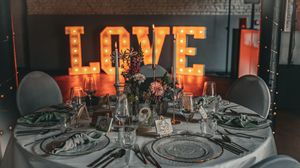 Elegant wedding reception tables with glowing LOVE marquee letters and romantic candlelight decor in a dimly lit venue.