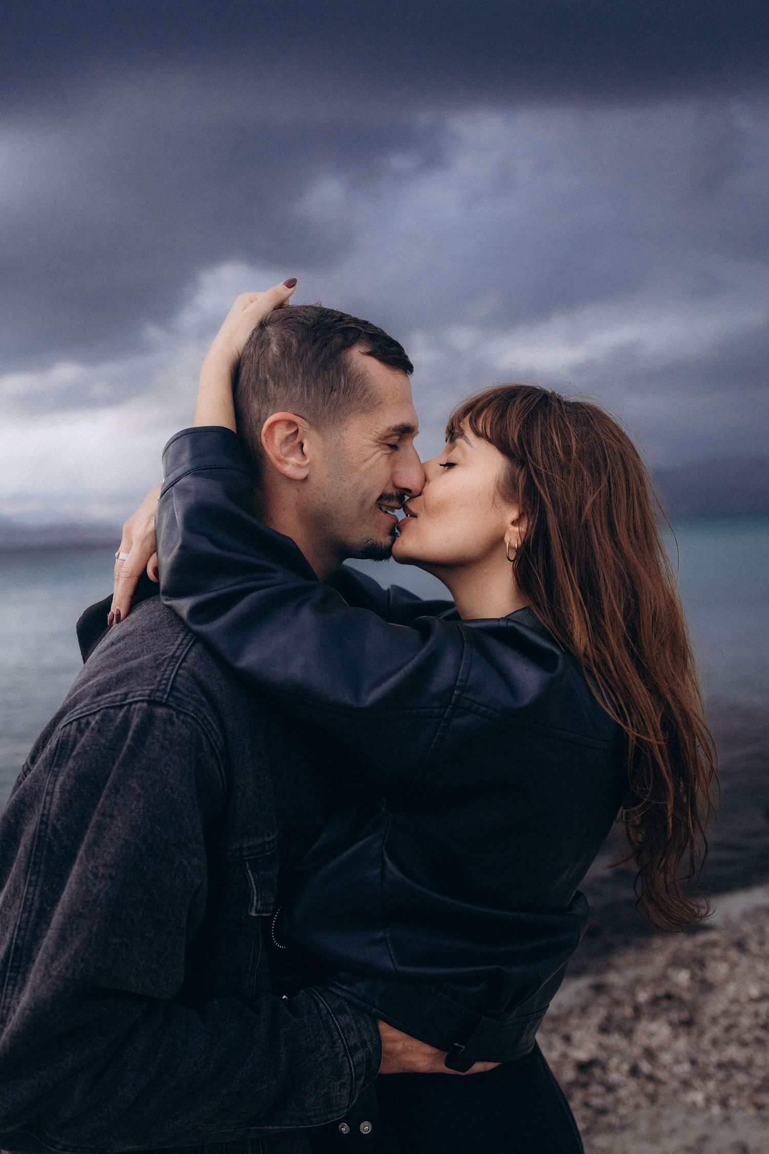 A romantic couple shares tender kisses against a moody, dark cloudy sky background in a series of intimate moments.