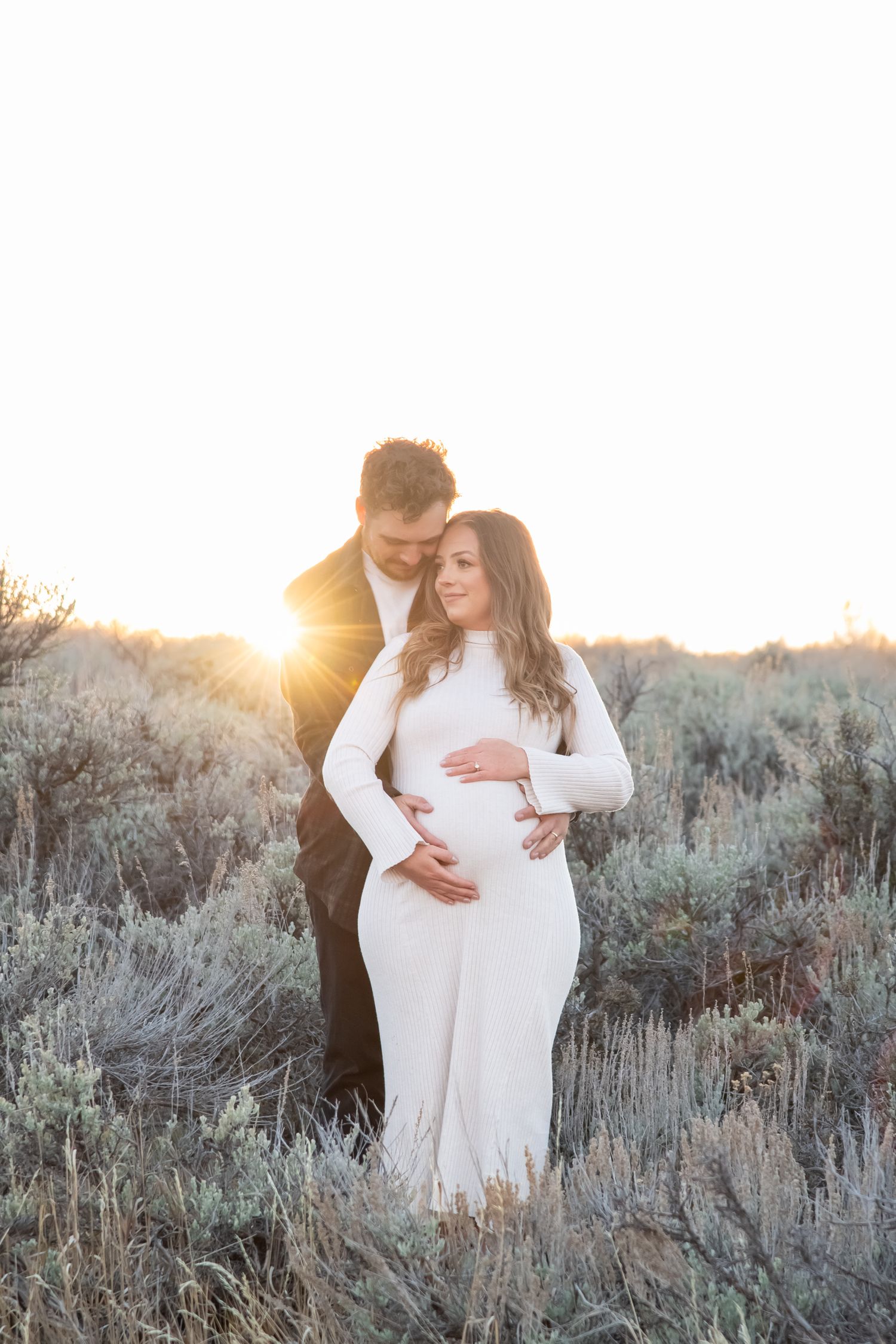 A couple embraces in Vail mountains among sagebrush at sunset during their maternity photo session.