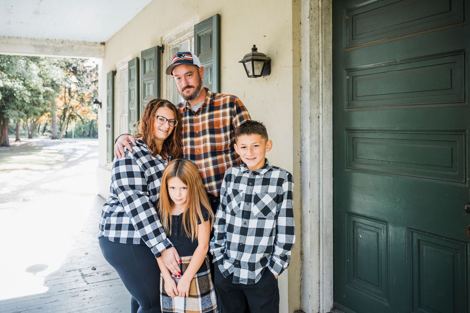 A family in coordinating plaid outfits poses together on a front porch for holiday photos.