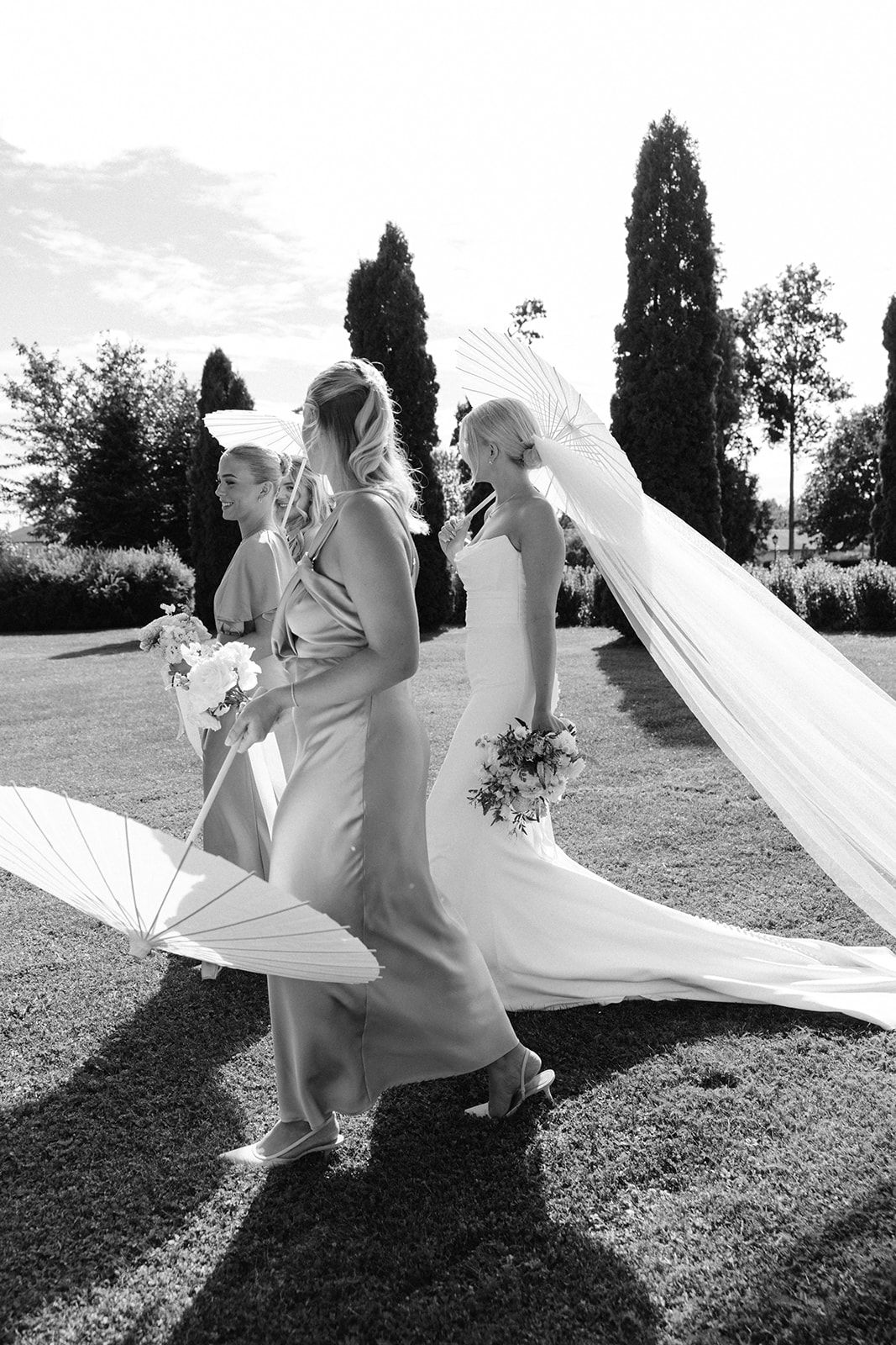 A flowing white wedding veil billows dramatically in the wind across a grassy hillside in black and white.