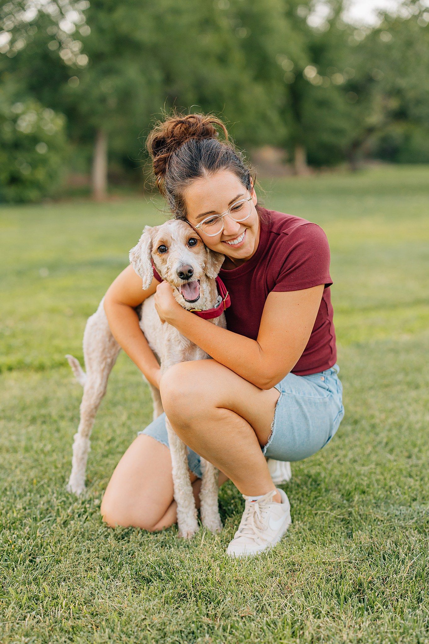 Anna is hugging her goldendoodle puppy who is looking at the camera. They are in a grassy field.