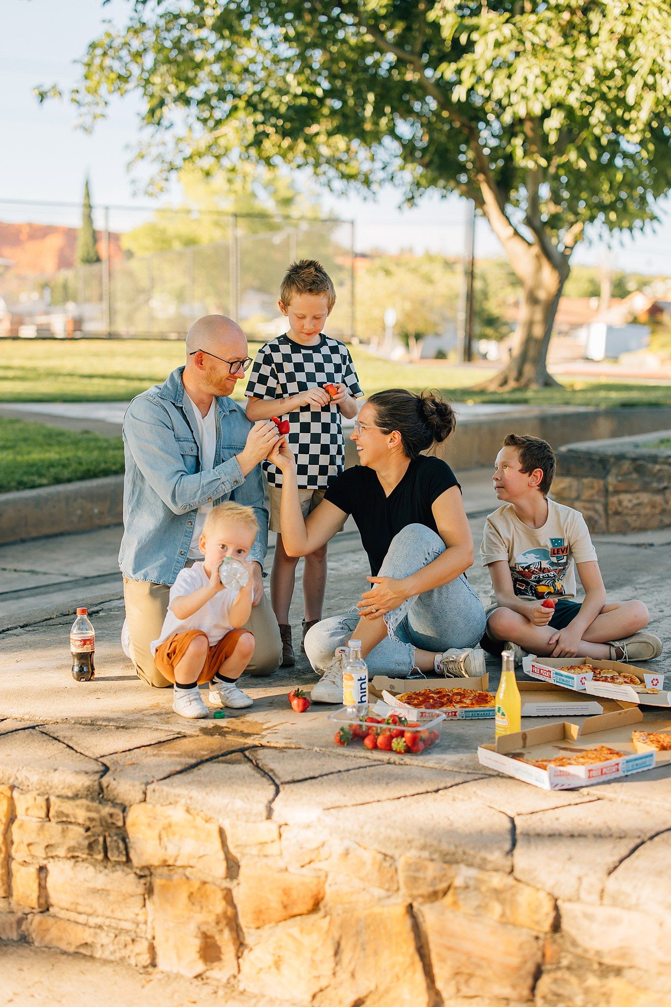 Anna's family laughing with each other eating a picnic with pizza and soda.